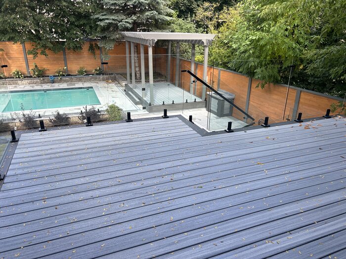 Elevated composite deck with glass railing overlooking a pool and pergola